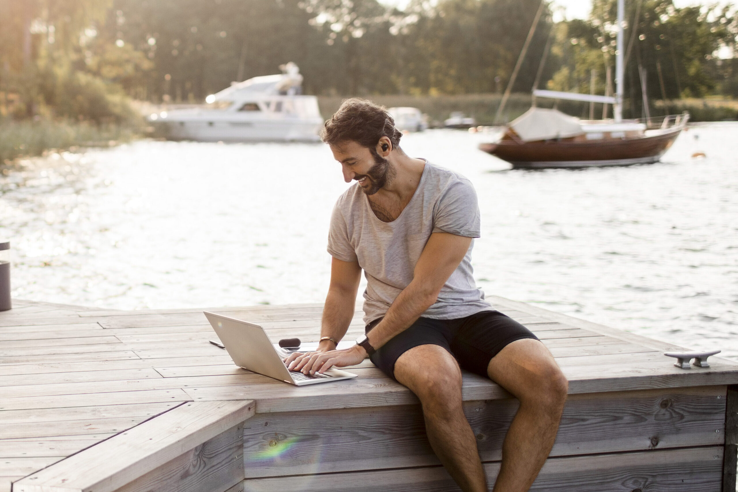 Male freelancer working on laptop at jetty | Smoobu