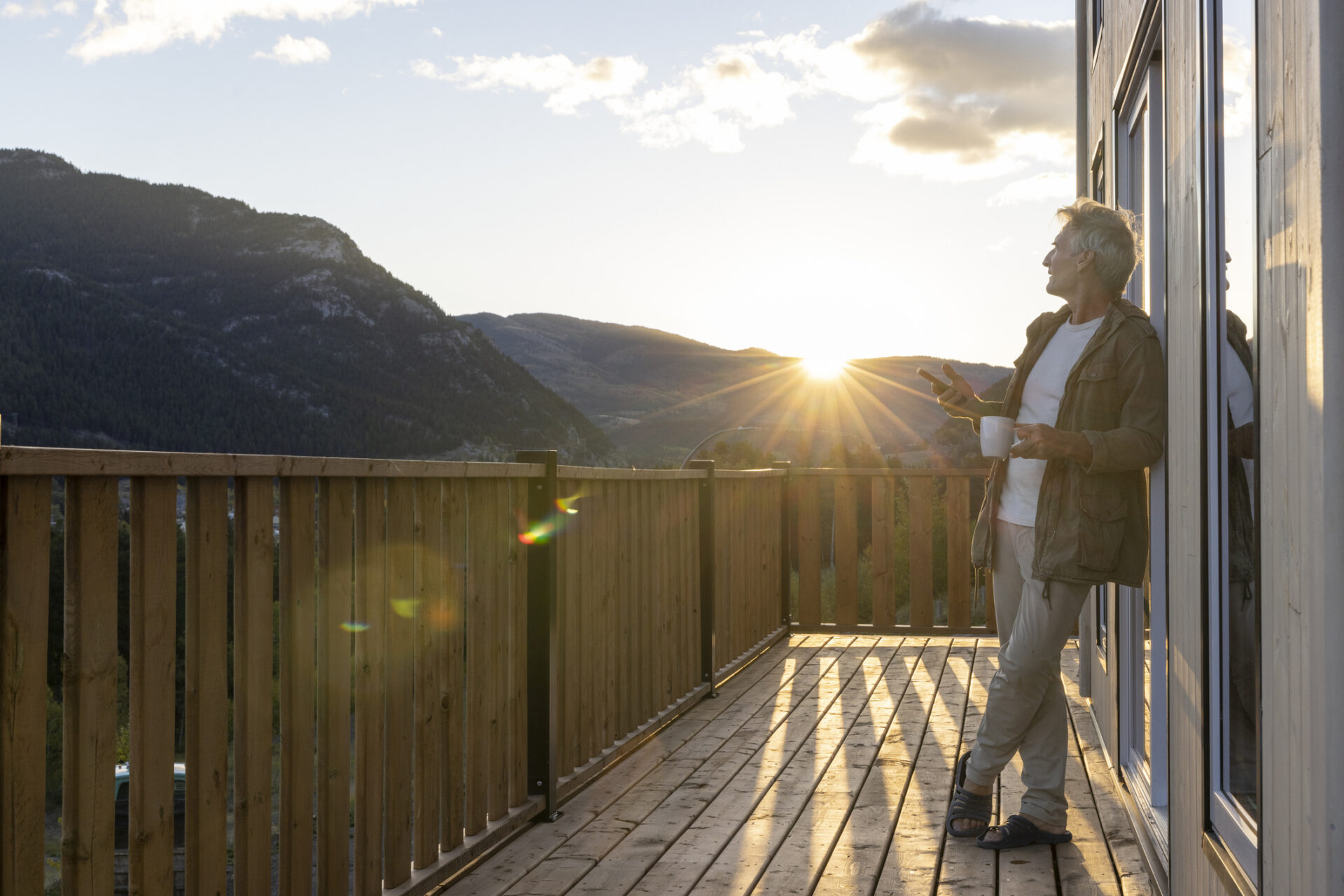Mature man watches sunrise from cabin deck with hot beverage | Smoobu