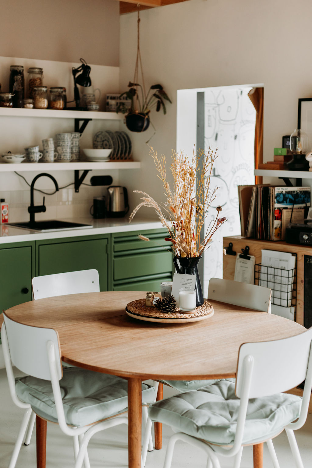 Kitchen with green cabinets, open shelves and a round dining table in a Familie Buitenhuys house